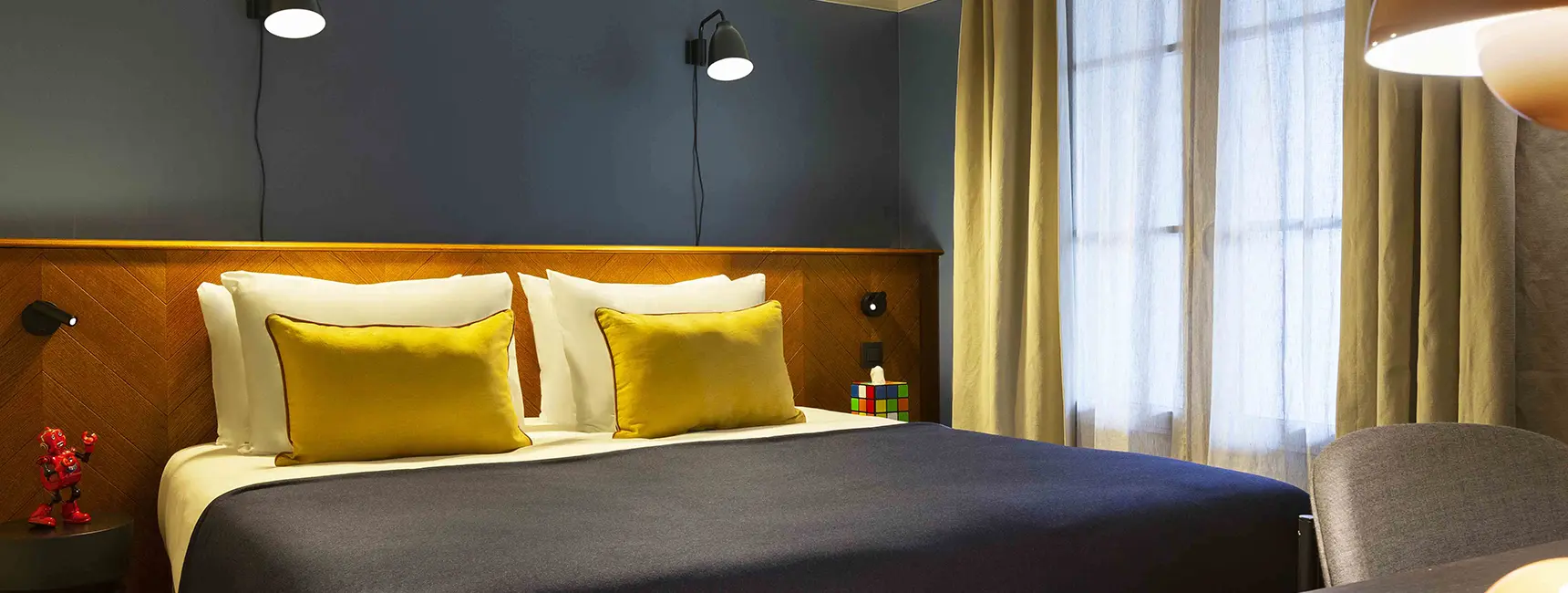 Lit double face à une grande fenêtre avec robot décoratif sur la table de chevet – penthouse RockyPop Grenoble