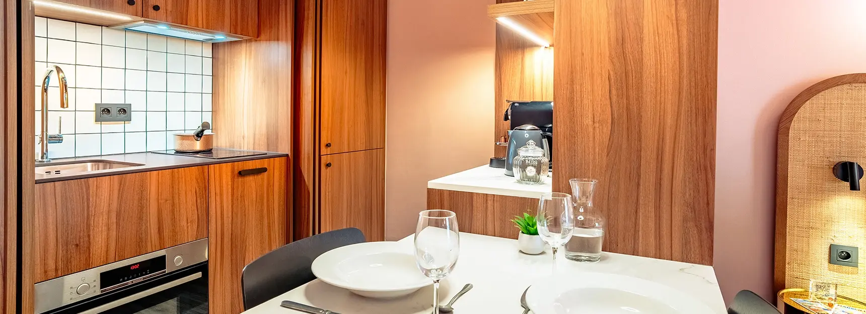 Table pour deux personnes au centre, lit double visible à droite, meuble de rangement au fond et cuisine toute équipée à gauche – RockyPop Marseille