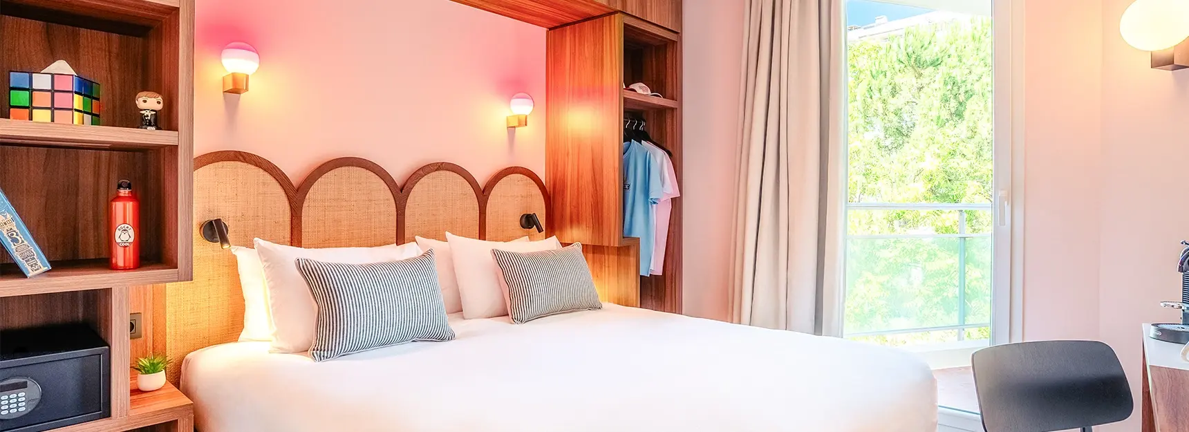 Lit double à gauche entouré de rangements, bureau avec chaise à droite et grande fenêtre lumineuse en fond – chambre RockyPop Marseille