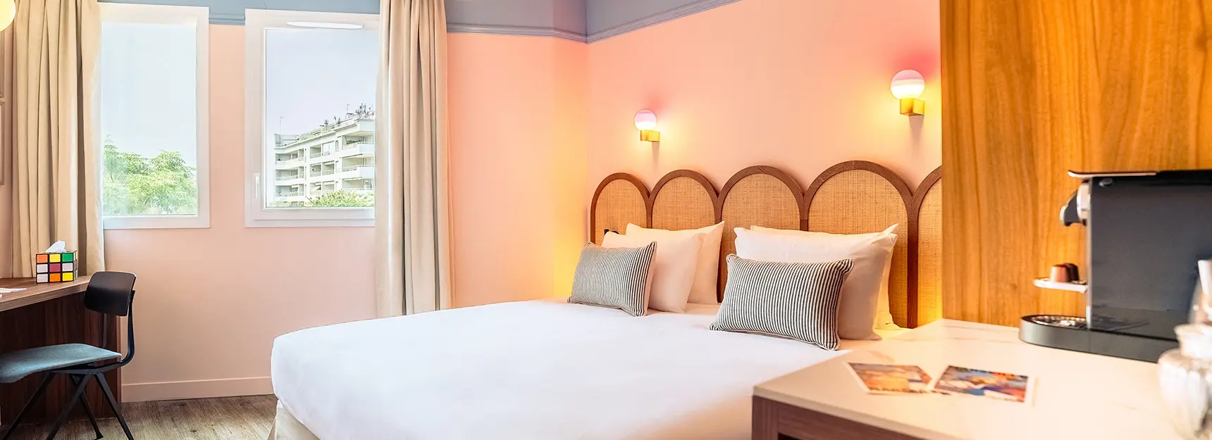 Vue sur lit double à droite, bureau avec chaise à gauche, grande fenêtre lumineuse en fond – chambre RockyPop Marseille