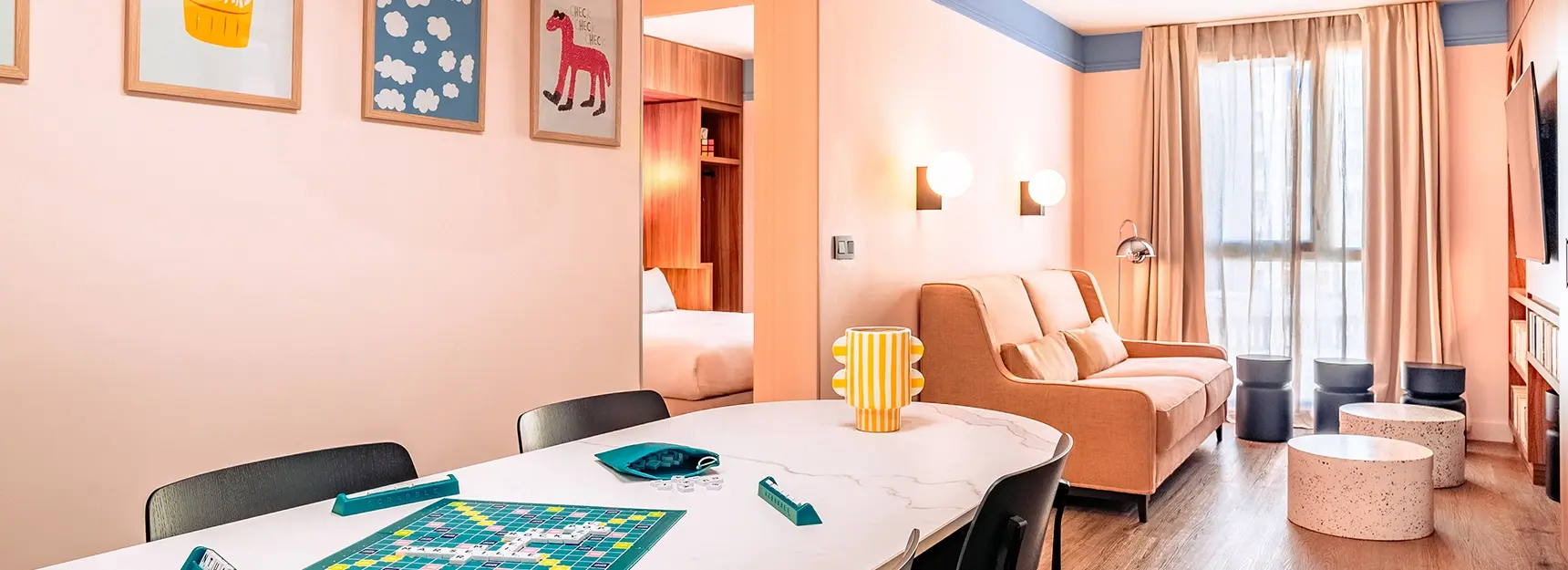 Pièce à vivre avec un jeux de société sur une grande table et un canapé au fond, et une chambre à gauche – RockyPop Marseille